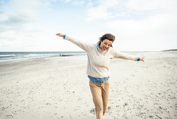 Portrait of young woman walking on sandy beach with raised arms