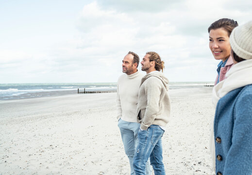 Group of adult friends standing and talking on coastal beach