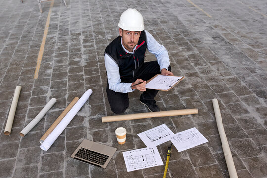 Male engineer holding site plan while kneeling on floor in building