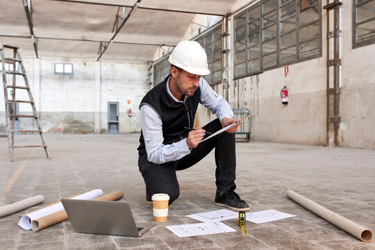 Male engineer analyzing site plan while kneeling on floor in building
