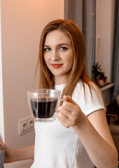 Woman hands holding mug of hot drink. She is smiling and holding a cup of coffee in hand split up in order to inhale the aroma of coffee. Beautiful Girl Drinking Coffee in home.