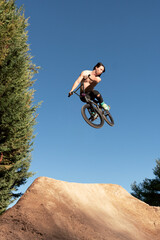 Fototapeta na wymiar Caucasian white boy jumping with long hair shirtless with BMX bike on a mountain in the field with sand and trees blue sky sunny day