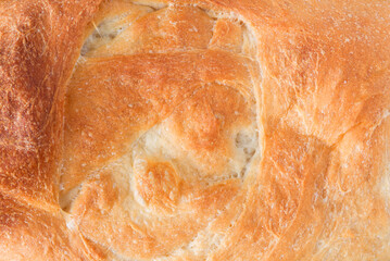 Overhead close view of the crust of a baked loaf of homemade bread illuminated with natural light.