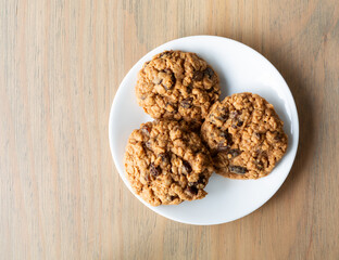 Top view of homemade oatmeal raisin cookies on a white plate atop a table illuminated with natural light.