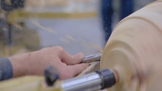 Carpentry, craftsmanship, design, manufacturing concept. Close up view - professional man carpenter using skew chisel for shaping piece of wood on woodturning lathe at workshop- super slow motion