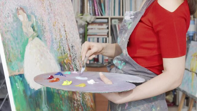Cropped shot of a female artist mixing paint on her palette while drawing. Creative woman enjoying writing a painting at her art studio. Painter drawing at the workshop