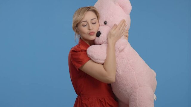 Young woman talking, hugging and kissing with a big teddy bear.Indoor studio shot isolated on blue background.
