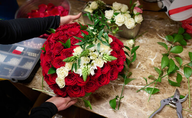 Florist making Flower box with red roses and white flowers on the table