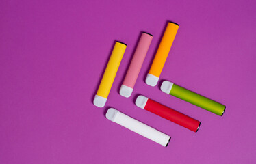 Colorful disposable electronic cigarettes on a purple background. The concept of modern smoking, vaping and nicotine. Top view.