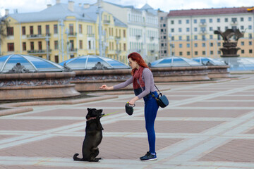 Naklejka premium Beautiful happy young woman with cute black dog have fun on street.