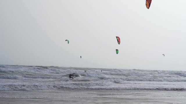 au ralenti, un kitesurf  saute au milieu des rouleaux de vagues sous un ciel jauni par les vents sahariens