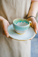 person in the apron holding handmade clay and turquoise cup of tea
