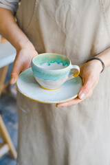 person in the apron holding handmade clay and turquoise cup of tea