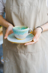 person in the apron holding handmade clay and turquoise cup of tea