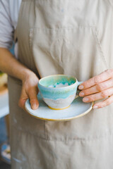 person in the apron holding handmade clay and turquoise cup of tea