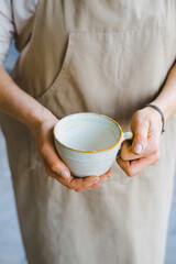 person in the apron holding handmade clay and turquoise cup of tea