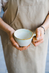 person in the apron holding handmade clay and turquoise cup of tea