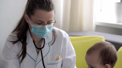 medicine and health, pediatrics, covid-19 concept - close-up young woman nurse or doctor pediatrician of Caucasian Slavic ethnicity examines infant 8-12 months baby on yellow gray sofa opposite window - Powered by Adobe