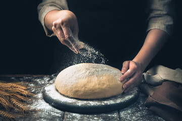 Sprinkling raw dough with your hand on a black background. Side view, horizontal.