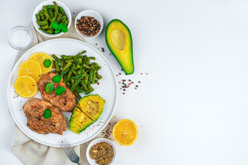 Fried chicken, fresh avocado and string beans on a white flat plate on a light background. The concept of culinary backgrounds. Top view with copy space.
