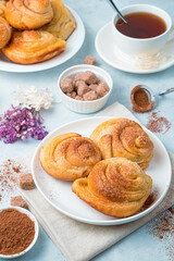 Fresh snail buns with cinnamon, cocoa and a cup of tea on a delicate blue background. Vertical orientation. The concept of baking.