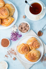 Delicate culinary background with fresh buns and tea on a light blue background. Top view, vertical. The concept of baking.