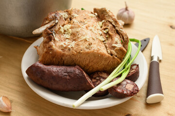 baked meat and blood sausage on a plate, green onion and garlic on wooden background, home cooking