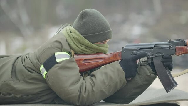 Side view of confident military woman aiming lying on tactical karemat outdoors. Portrait of professional beautiful Caucasian female soldier training on polygon.