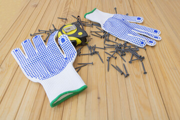 Black Screws on wooden background - protective gloves and Yellow measuring tape. Hardware for construction