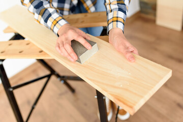 Close-up shot of a woman at home sanding a wood on a workbench