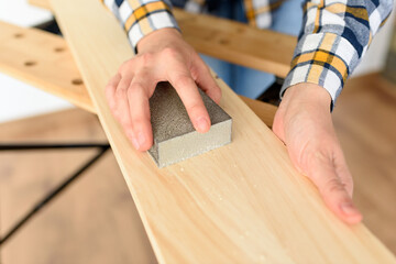 Close-up shot of a woman at home sanding a wood on a workbench