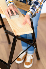 Close-up shot of a woman at home sanding a wood on a workbench
