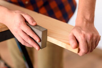 Close up shot of a man at home sanding wood on a workbench.