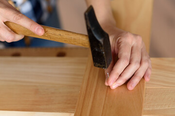 Close up of young woman assembling furniture at home working with hammer. DIY concept