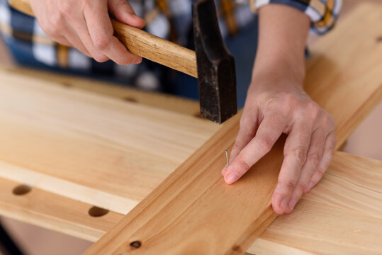 Close up of young woman assembling furniture at home working with hammer. DIY concept