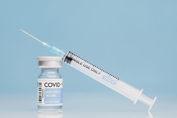 Medical syringe and glass vial with coronavirus vaccine placed against blue background