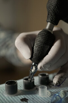 Closeup of crop unrecognizable tattooist dipping tattoo machine in black ink while working in salon