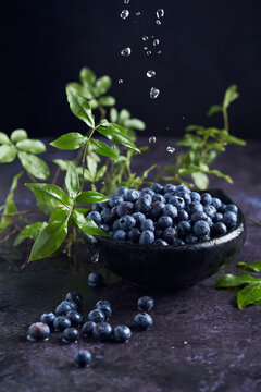 From above of bowl with pile of ripe healthy washed blueberries placed on black marble table with green leaves in kitchen