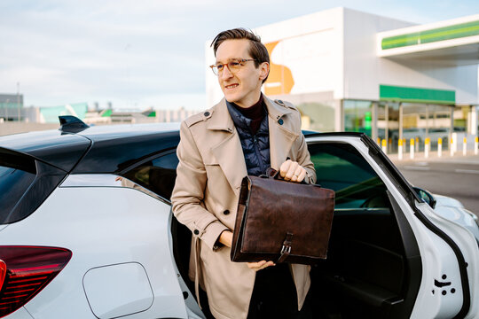 Confident male entrepreneur in coat and with attache case getting out of modern automobile and looking away