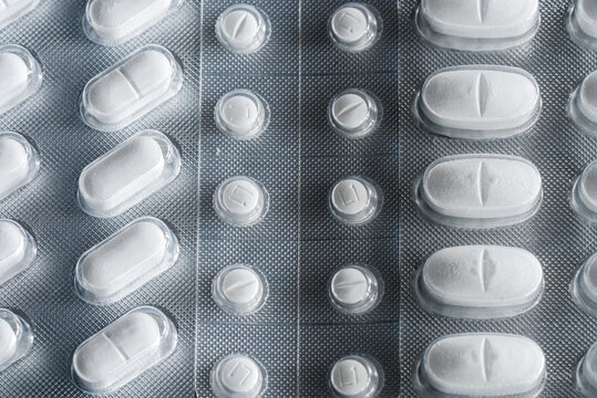 Closeup top view of full frame background of various white pills in plastic blisters arranged in row