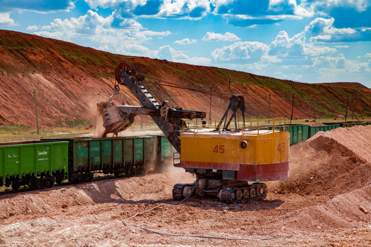 Arkalyk, Kazakhstan - May 15, 2012: Aluminium ore mining and transporting. Bauxite clay Open-cut mining. Loading ore with electrical excavator in hopper car train, on blue sky with clouds.