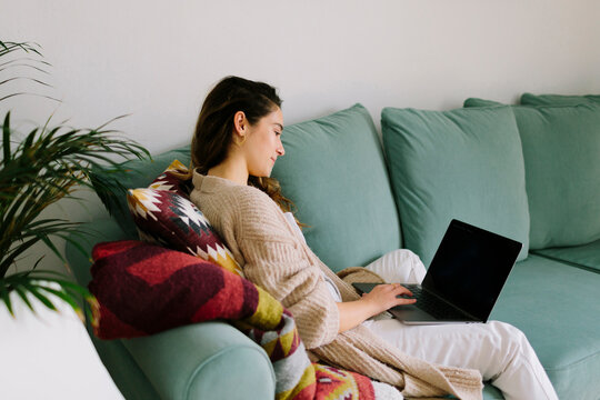 Pensive Woman Sitting On Sofa Working With Laptop