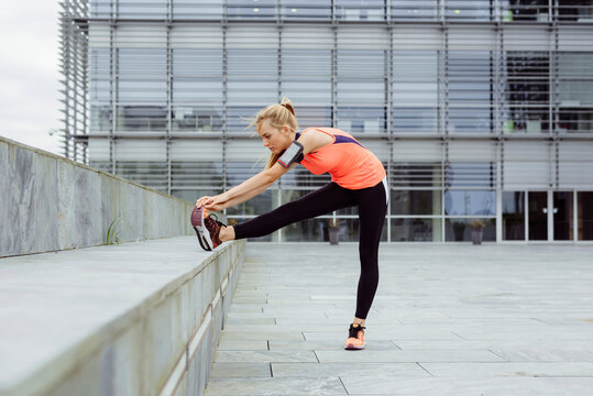 Side view of pretty blonde young woman stretching on the street before running