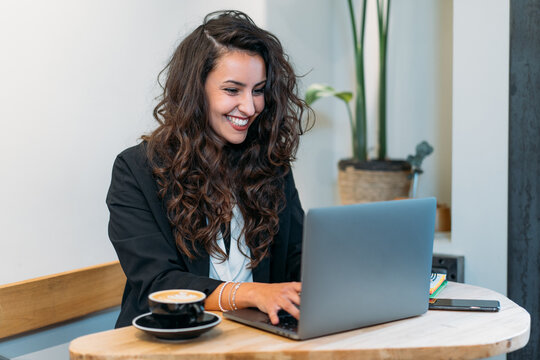 Charming female entrepreneur sitting at table whit coffee in a mug browsing laptop while working on project remotely in cafe