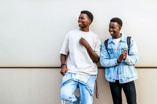 Cheerful young African American friends in casual clothes looking off to the side on a city wall.