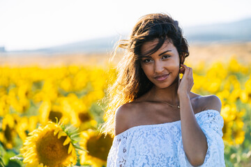 Happy ethnic female standing with raised arms in booming sunflower field and looking at camera