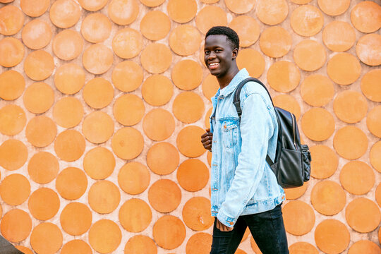 Young black man with denim jacket and backpack looking at the camera while walking