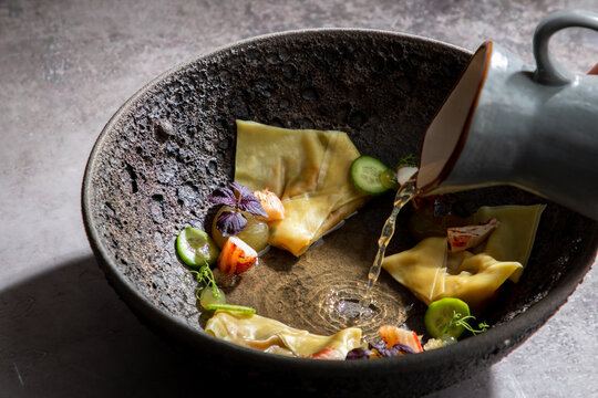 Crop anonymous cook adding broth into bowl with traditional Japanese dumplings while preparing meal in restaurant