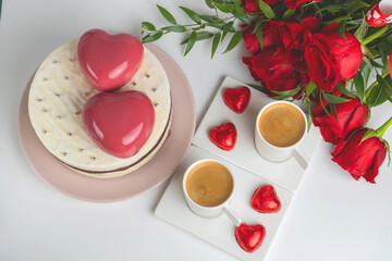 mousse cake in white glaze with two big pink hearts, two cups of coffee and a bouquet of red roses