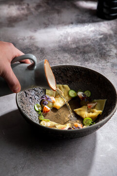 Crop anonymous cook adding broth into bowl with traditional Japanese dumplings while preparing meal in restaurant